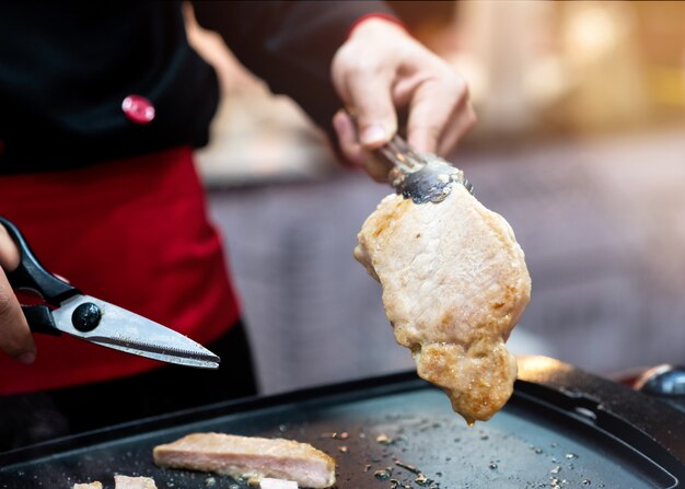 Le chef est un steak de porc grillé, des ciseaux à main coupant un steak de porc grillé