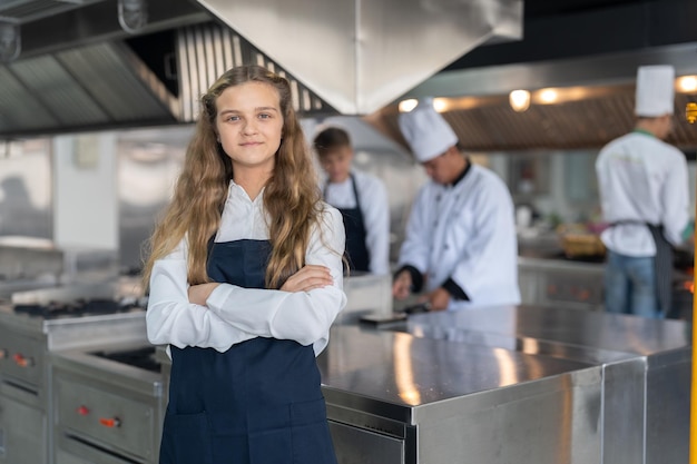 Photo chef étudiante portant un tablier debout avec les bras croisés étudiant la cuisine dans une école de cuisine