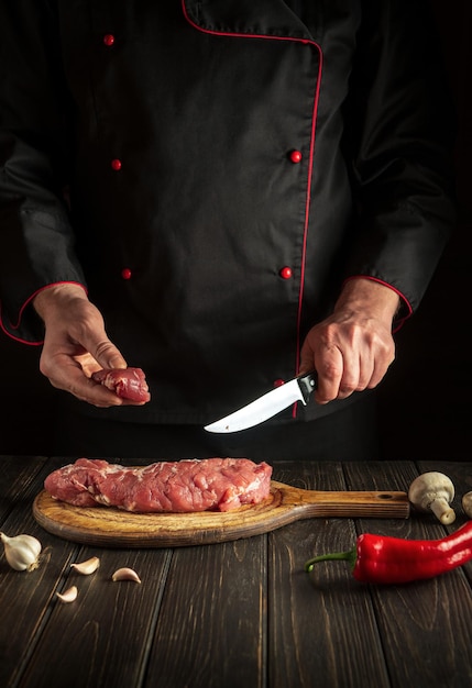 Un chef expérimenté coupe de la viande de veau crue sur une planche à découper avant le barbecue