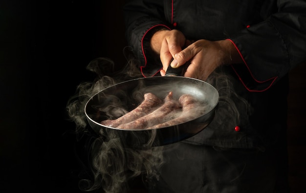 Le chef fait frire des saucisses sur une poêle chaude avec de la vapeur Menu ou concept de recette pour hôtel sur fond noir