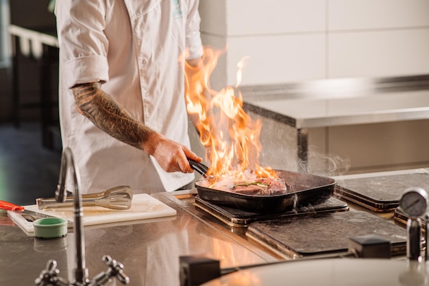 Le chef fait frire un steak avec un feu dans la cuisine du restaurant