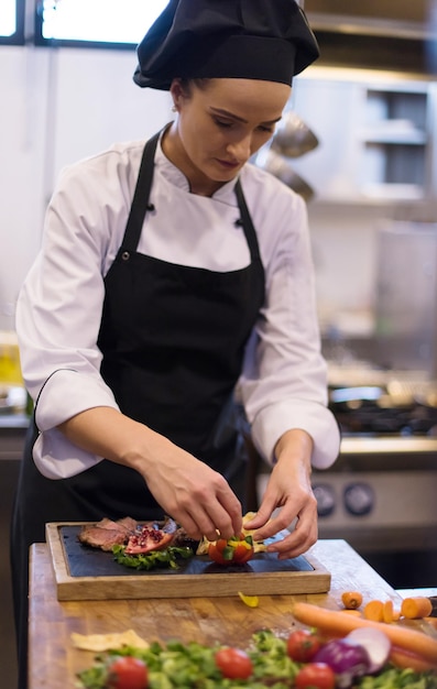 Chef féminin dans la cuisine d'un hôtel ou d'un restaurant préparant un steak de boeuf avec une décoration végétale