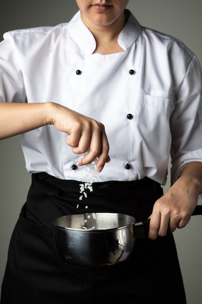 Chef femme saupoudrer de sel cuisson préparer assaisonnement des aliments sur fond gris