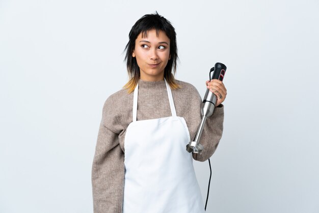 Chef fille à l'aide d'un mélangeur à main sur un mur blanc et debout sur le côté