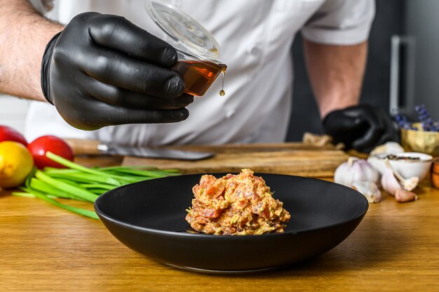 Le chef en gants noirs prépare du tartare à partir de thon frais