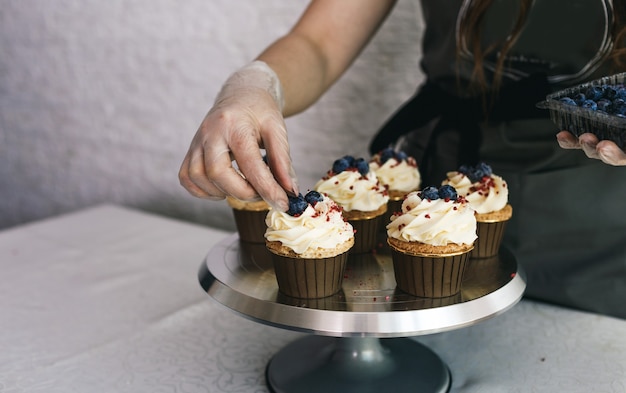 La chef girl décore des cupcakes frais recouverts de crème à la vanille avec des baies. Petits gâteaux faits maison sucrés avec de la crème sur un plateau.