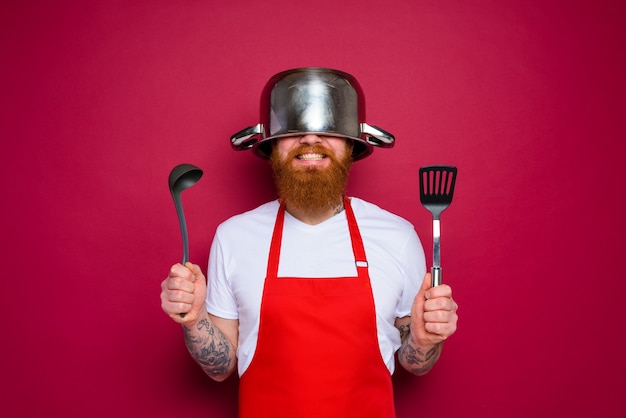 Le chef heureux avec la barbe et le tablier rouge est prêt à cuisiner