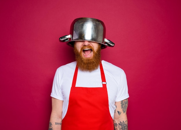 Le chef heureux avec la barbe et le tablier rouge joue avec le pot