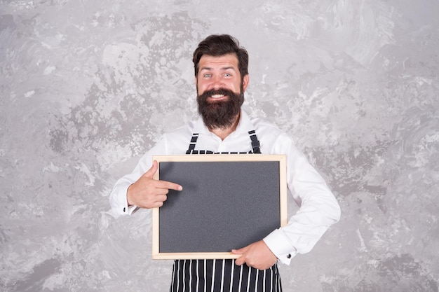 Chef d'homme barbu brutal présentant le menu du restaurant sur un tableau vide pour l'annonce publicitaire de l'espace de copie