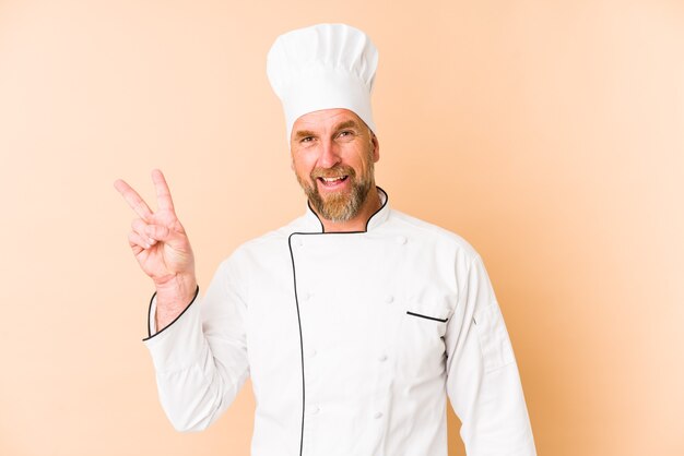 Chef homme isolé sur fond beige joyeux et insouciant montrant un symbole de paix avec les doigts.