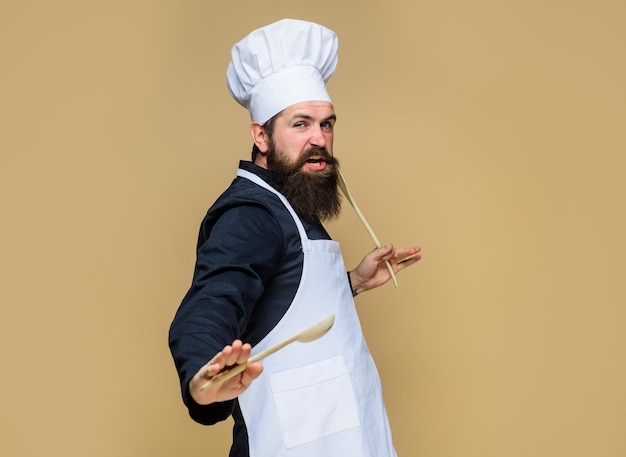 Chef homme en uniforme de cuisinier avec cuillère en bois et spatule à la main beau chef cuisinier avec cuisine