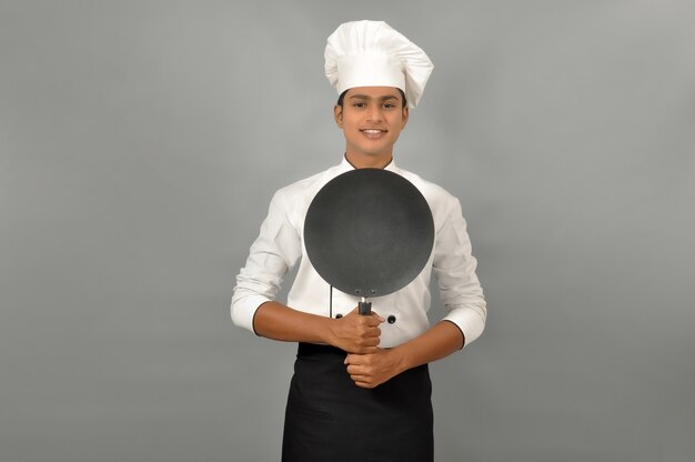 Chef indien souriant confiant souriant derrière la poêle à frire sur fond gris