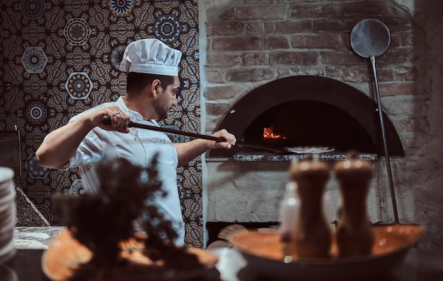 Le chef italien met une pizza gastronomique fraîchement préparée dans le four à pierre.
