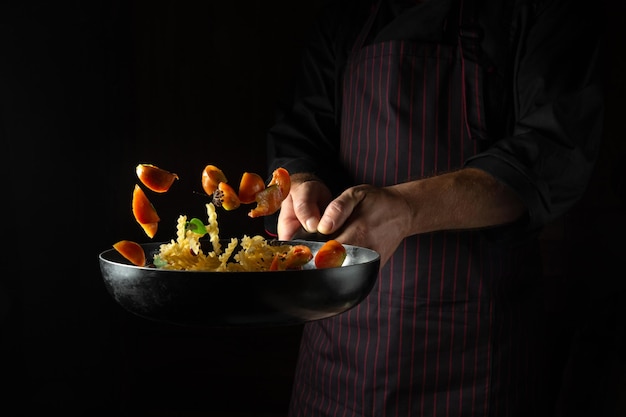 Le chef jette de la nourriture sur une poêle chaude Pâtes alimentaires de rue thaïlandaises aux épices et légumes Espace pour la publicité sur fond sombre