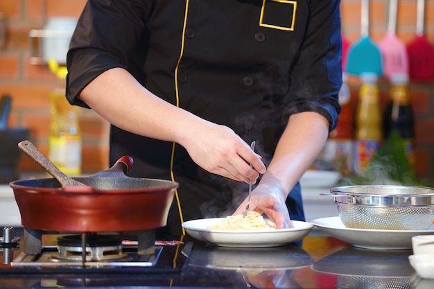 Chef de main CloseUp cuisson spaghetti près de casserole sur la cuisinière à gaz dans la cuisine