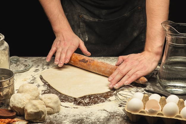 Chef mains roulent la pâte sur une table en bois avec de la farine de blé