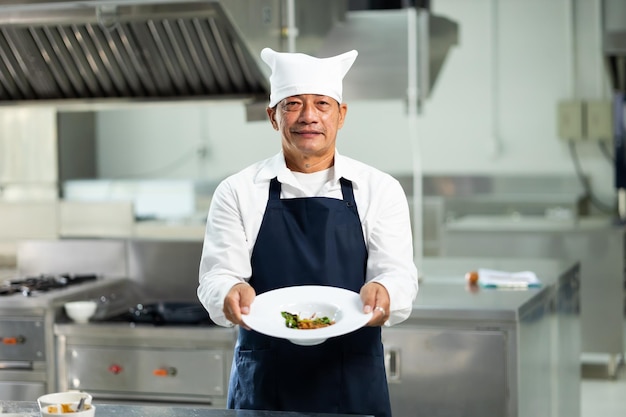 Chef maître mature regardant la caméra et battant le portrait de la classe de cuisine chef professionnel asiatique thaïlandais de sexe masculin repas de cuisine salle de classe de cuisine cours d'école de cuisine dans une école de cuisine