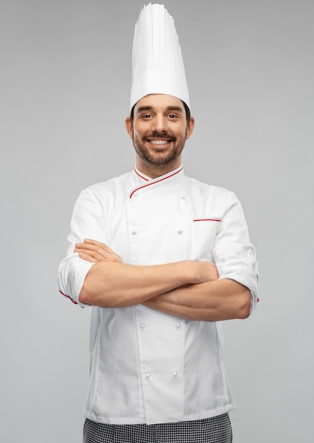 un chef mâle heureux et souriant en toque avec les bras croisés