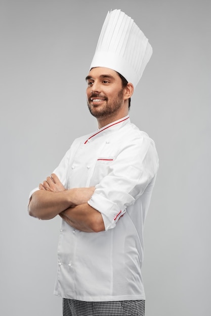 un chef mâle heureux et souriant en toque avec les bras croisés