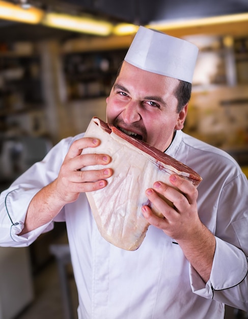 Chef mangeant une grosse tarte de viande crue dans la cuisine. Portrait en gros plan d'un bel homme avec de la viande crue dans la cuisine. Manger de la viande. Un chef masculin affamé va manger de la viande crue