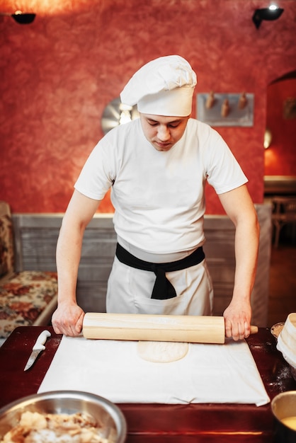 Chef masculin étaler la pâte avec un rouleau à pâtisserie sur une table en bois. Cuisine de strudel maison