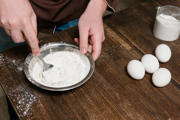 Le chef mélange de la farine avec des œufs dans un bol sur une table en bois, vue de dessus du concept de préparation des aliments