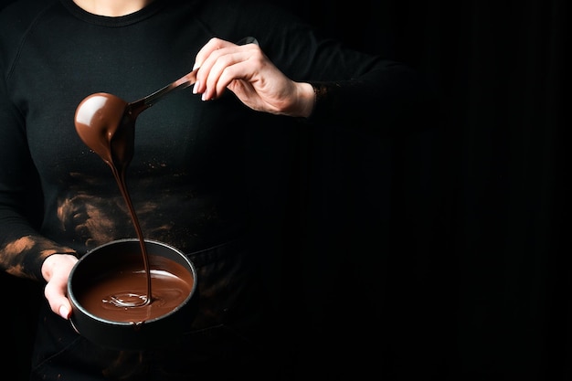 Le chef met du chocolat chaud dans un bol sur un fond noir Préparation du chocolat