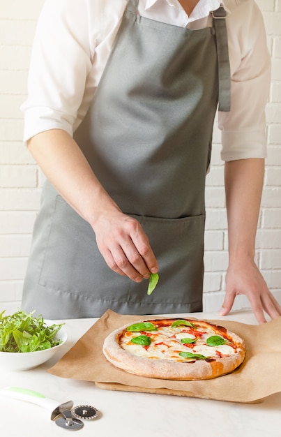 Le chef met des feuilles de basilic vert sur la pizza.