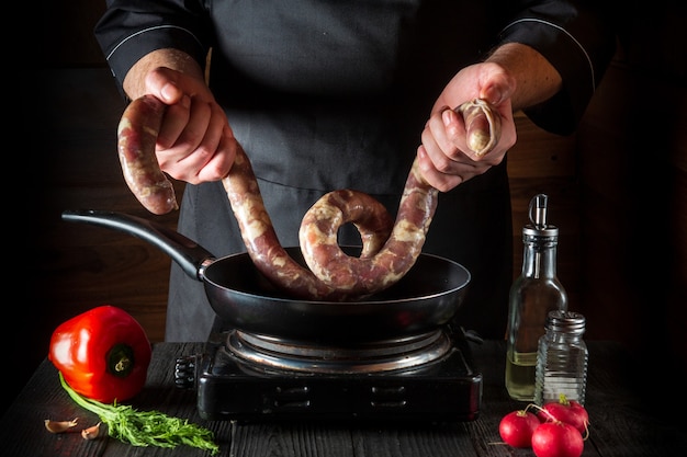 le chef met la saucisse de viande crue dans la casserole avant de cuisiner l'environnement de travail dans la cuisine du restaurant