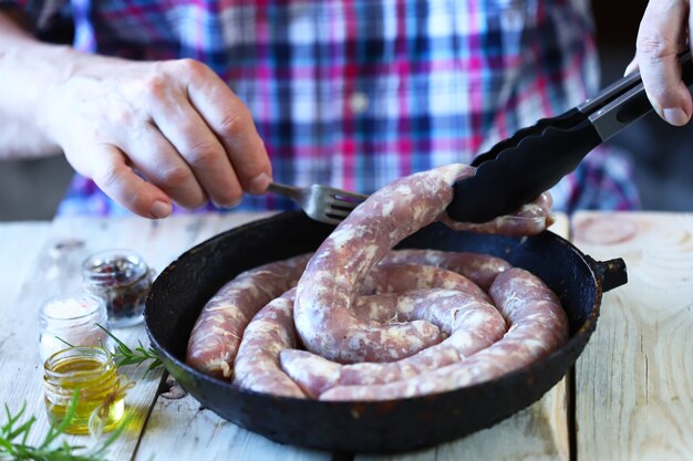 Le chef met les saucisses crues dans une poêle