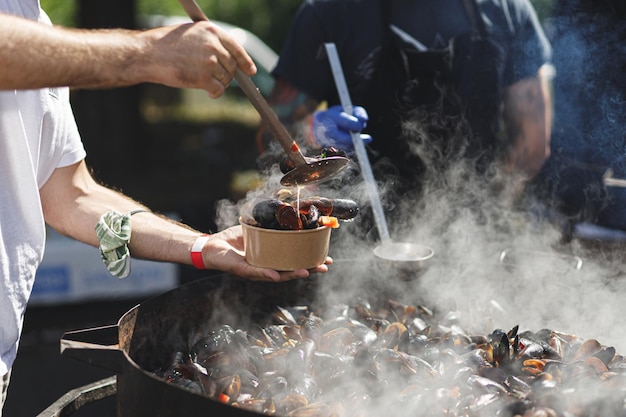 Chef mettant de délicieuses moules bouillies dans une boîte à emporter cuisinant des fruits de mer au festival de l'alimentation de rue