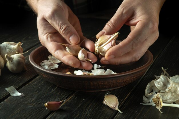 Le chef nettoie l'ail dans une assiette vintage sur la table de la cuisine avant de préparer un repas végétarien