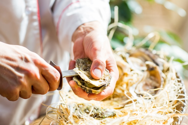 Le chef ouvre des huîtres fraîches dans un restaurant