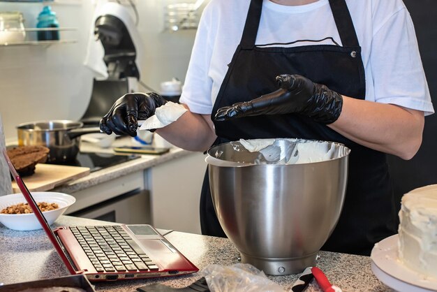 Chef pâtissier cuisinier confiseur ou boulanger en gants noirs fait un gâteau et à l'aide d'un ordinateur portable Blogueur alimentaire