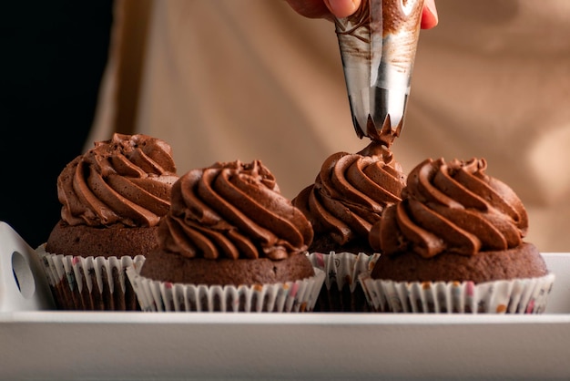 Le chef pâtissier décore les cupcakes avec de la crème au chocolat de la poche à douille Muffins au cacao faits maison en gros plan