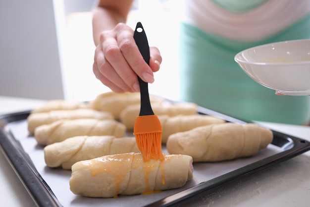 Chef pâtissier enduisant le jaune d'oeuf sur un petit pain cru avec un pinceau en silicone en gros plan