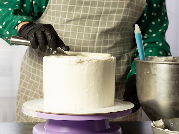 Le chef pâtissier réalise un gâteau à la crème blanche à l'aide d'une spatulealigner les bords du gâteau