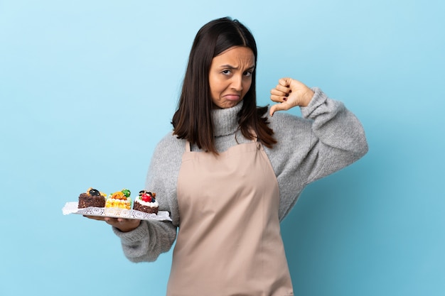 Chef pâtissier tenant un gros gâteau sur bleu isolé fier et satisfait de lui-même