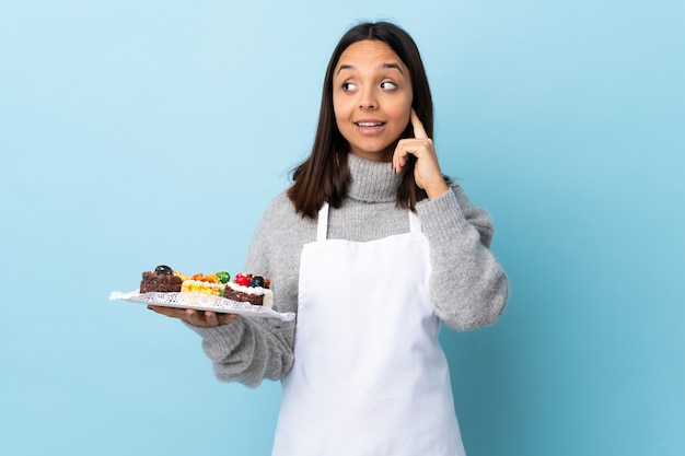 Chef pâtissier tenant un gros gâteau sur un espace bleu isolé en riant