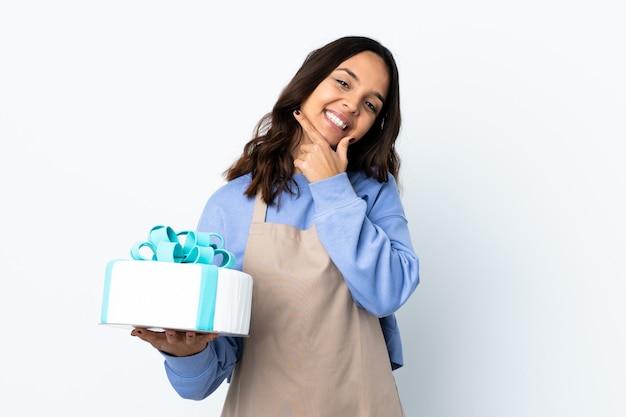 Chef pâtissier tenant un gros gâteau sur fond blanc isolé heureux et souriant