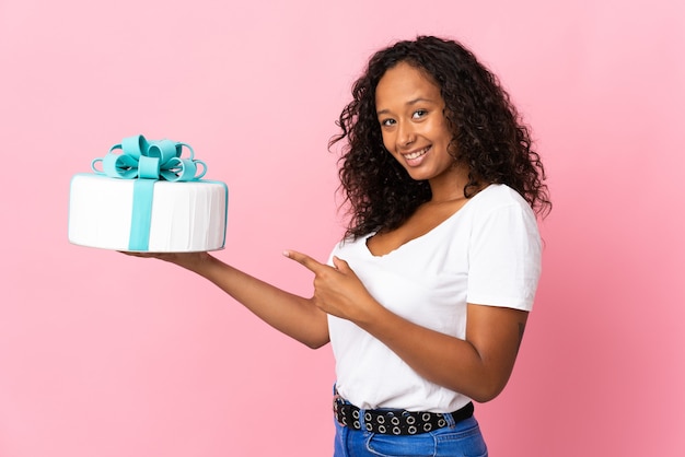 Chef pâtissier tenant un gros gâteau isolé sur fond rose et le pointant