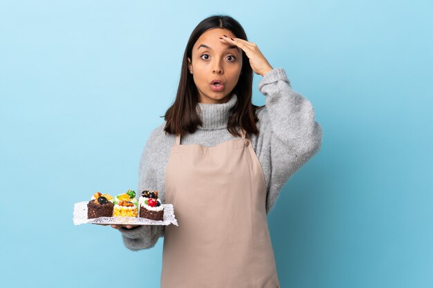 Chef pâtissier tenant un gros gâteau sur un mur bleu isolé a réalisé quelque chose et a l'intention de la solution