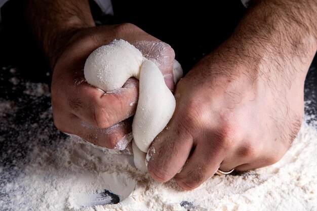 Le chef pétrit la pâte sur un fond sombre, la table est parsemée de farine