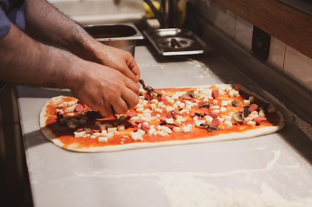 Le chef de pizza a mis la sauce sur la base dans une cuisine commerciale