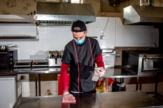 Chef portant un masque médical désinfectant la table de travail avec un antiseptique