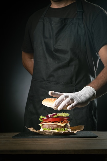 Chef préparant un hamburger sur fond noir.