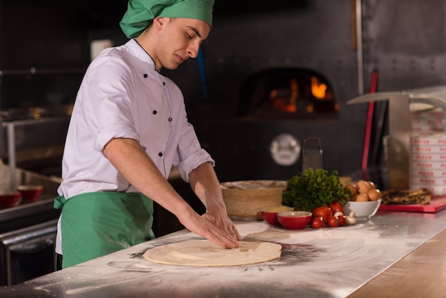 chef préparant la pâte à pizza roulant avec les mains saupoudrées de table de farine