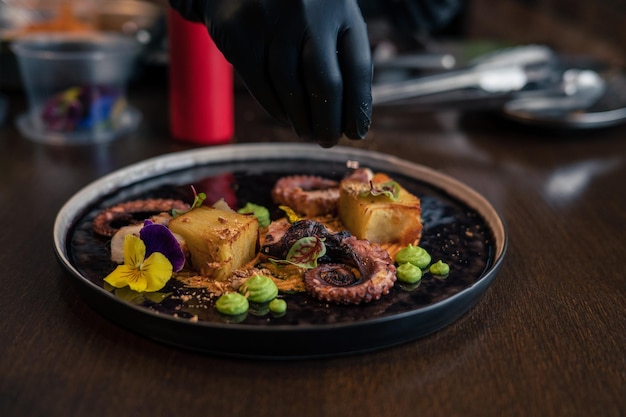 Chef préparant une pieuvre avec des pommes de terre sur une purée de pois décorée de fleurs comestibles