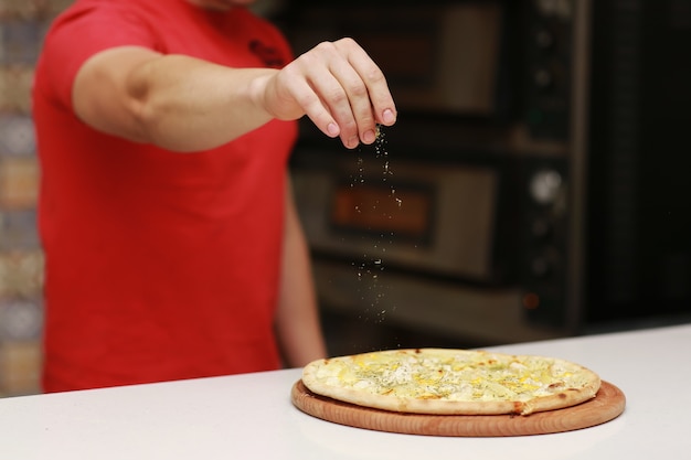 Le chef prépare la pizza et l'arrose d'épices