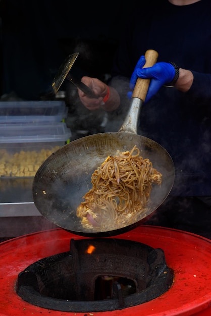 Un chef prépare des plats chinois lors d'un festival de cuisine de rue photographié alors que la nourriture vole au-dessus d'une poêle remplie de feu et de fumée